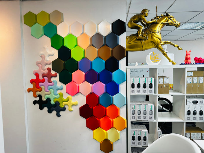 3D printer filament color samples displayed in hexagonal and puzzle-piece shapes showing rainbow spectrum of PLA colors with product shelf.