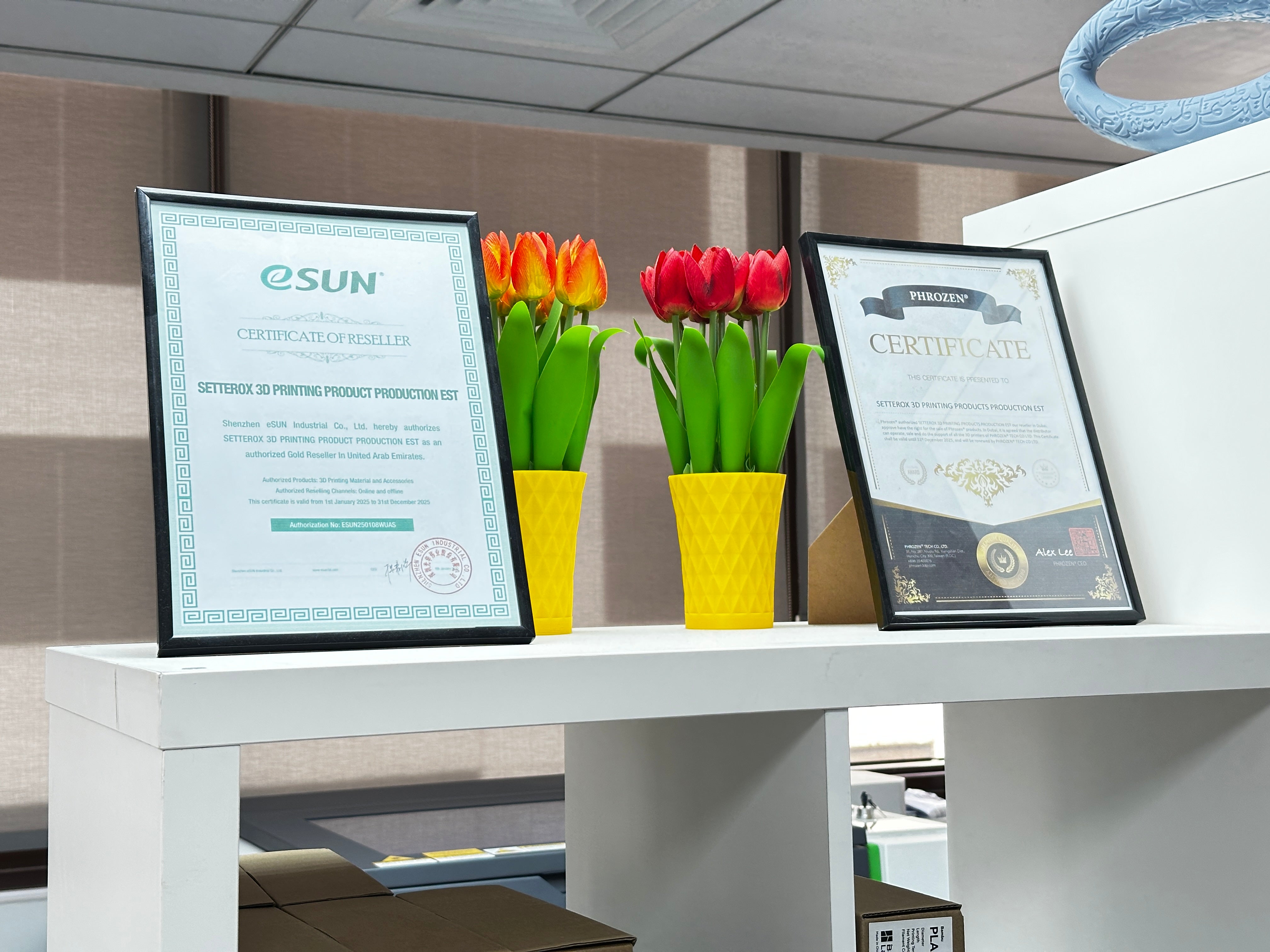 Official authorized reseller certificates from eSUN and Phrozen for 3D printing products displayed with decorative 3D printed tulips in yellow vases